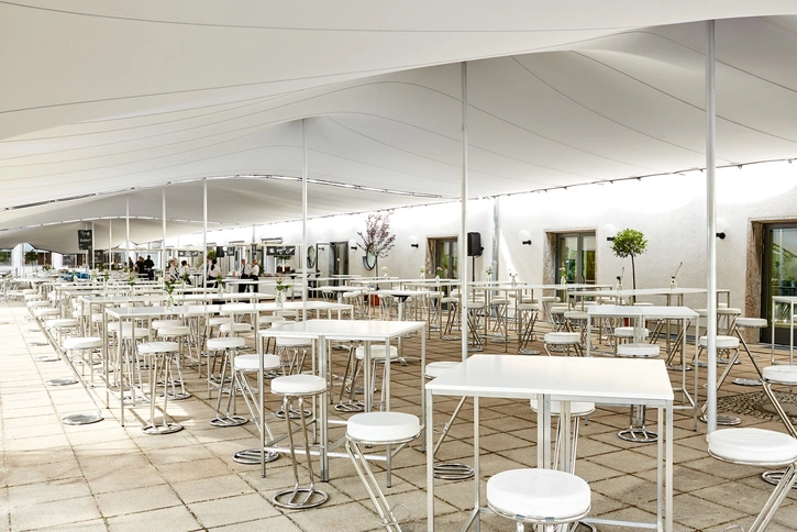Terrasse mit weißen Stehtischen und Hockern unter einem großen weißen Zeltdach