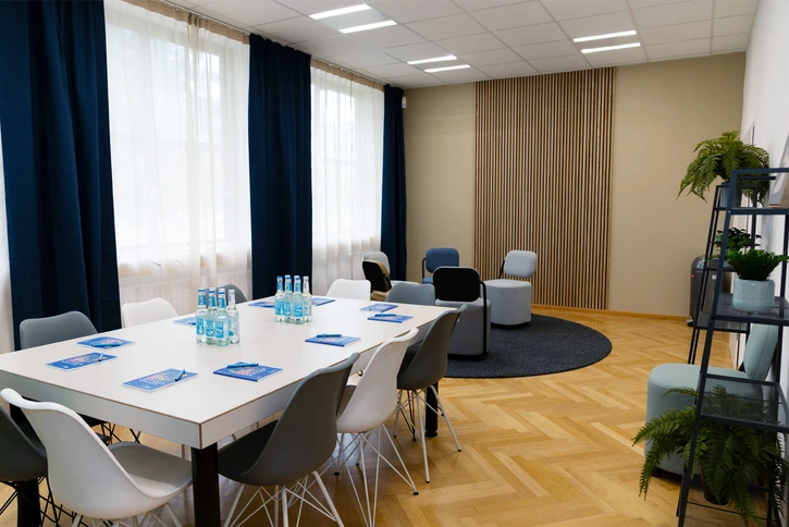 Meitner-Raum: Gemütlicher Raum mit Tisch und 10 Stühlen, Sitzgruppe im Hintergrund und Pflanzen-Regal